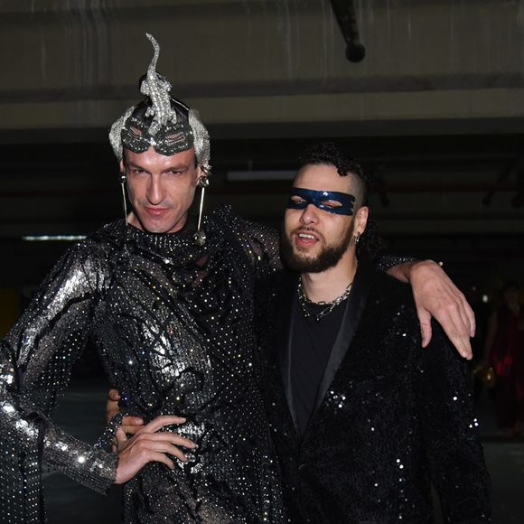 Dudu Bertholini ousou em um look futurista repleto de cristais e aplicações metálicas, acompanhado de adereço de cabeça escultural, enquanto o parceiro seguiu no clássico preto com toques de brilho