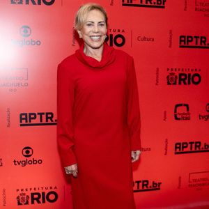 Arlete Salles: A veterana atriz esbanja elegância em um vestido longo inteiramente vermelho de silhueta reta e mangas compridas, caracterizado por uma gola boba volumosa e discreta. Ela complementa o visual minimalista com sapatos pretos de salto baixo e joias delicadas