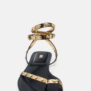 Detalhes que fazem diferença: a sandália rasteira da Zara de R$ 279 combina tiras delicadas com aplicações metálicas em concha, além de fechamento no tornozelo com fivela, garantindo ajuste firme e estilo refinado