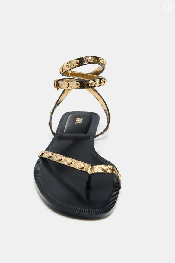 Detalhes que fazem diferença: a sandália rasteira da Zara de R$ 279 combina tiras delicadas com aplicações metálicas em concha, além de fechamento no tornozelo com fivela, garantindo ajuste firme e estilo refinado