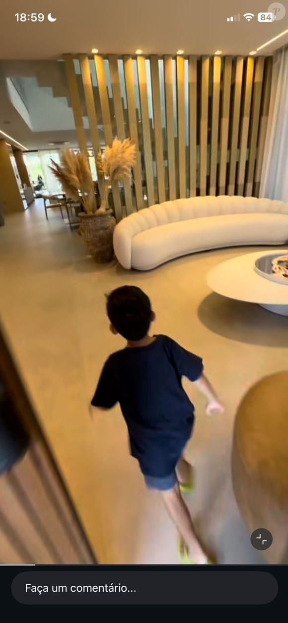 Na sala, um sofá curvo imponente se torna o grande protagonista do décor, dialogando com a mesa de centro orgânica e com o painel ripado vertical que separa os ambientes sem bloquear a luz natural