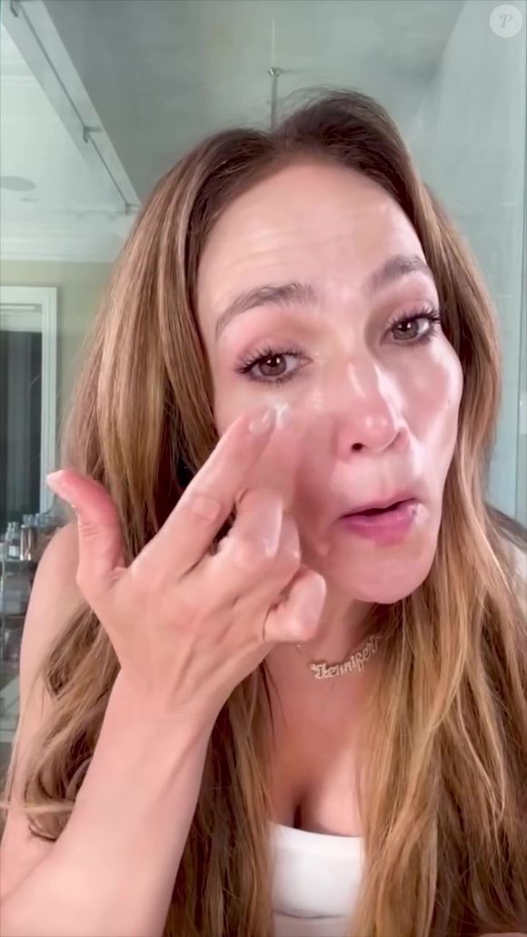 Jennifer Lopez aplica um produto, que parece ser creme ou sérum, na área dos olhos, provavelmente, para suavizar olheiras