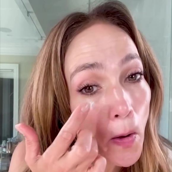 Jennifer Lopez aplica um produto, que parece ser creme ou sérum, na área dos olhos, provavelmente, para suavizar olheiras