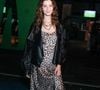 Giselle Batista aposta em um slip dress midi acetinado com estampa de animal print de leopardo, sobreposto por uma jaqueta oversized de couro preto com modelagem despojada. O visual ganha ares urbanos com botas pretas de cano médio e saltos estruturados, além de um mix de colares de correntes sobrepostos