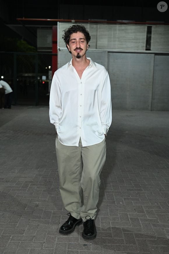Jhonny Massaro apostou na elegância despretensiosa com uma camisa de seda fluida branca com os botões superiores abertos, criando um decote V suave. O ator combinou a peça com uma calça chino bege de caimento reto e folgado e sapatos sociais pretos de solado grosso. A produção destacou seu estilo autoral, minimalista e sofisticado
