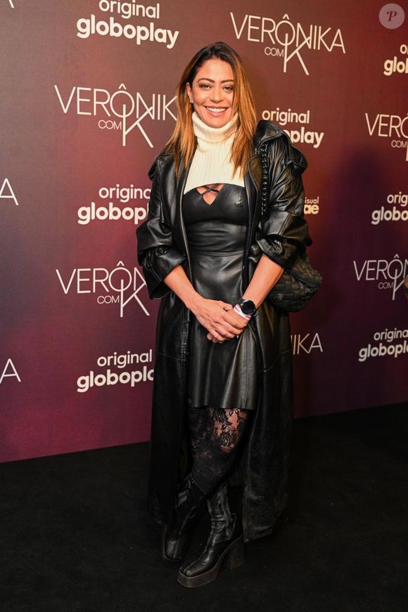 Carol Castro usou um vestido tubinho preto sob uma sobreposição de tricô gola alta off-white com recorte curto no peito. Por cima, veste um sobretudo de couro sintético preto de comprimento longo. A produção é arrematada por meia-calça rendada com estampas florais pretas, botas de couro de salto grosso e uma bolsa tiracolo estruturada preta
