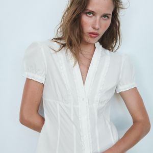 A Camisa de Popelina com Abertura e Laços da Zara tem modelagem ajustada, gola redonda, manga curta e detalhes de abertura e laços na parte frontal