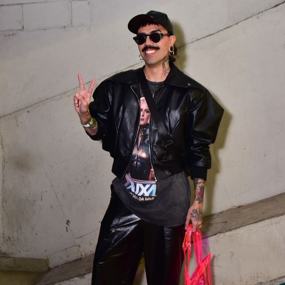 Edu apostou em uma produção streetwear conceitual composta por jaqueta de couro preta e bermuda ampla de mesmo material. Por baixo, vestiu camiseta vintage com estampa temática do show "Xuxa - O Último Voo da Nave", somada a óculos escuros e boné