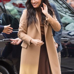 Meghan Markle mostra outra possibilidade de styling ao combinar tons terrosos e alfaiataria, com trench coat bege ou camelo, blusa de tricô marrom-café e saia midi de cetim marrom-fechado