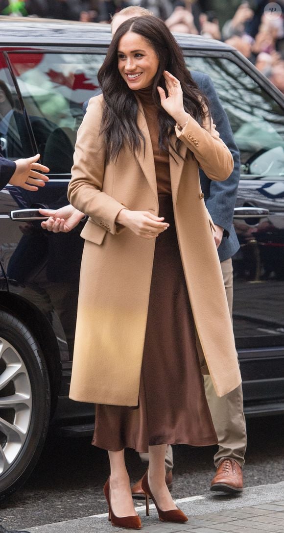 Meghan Markle mostra outra possibilidade de styling ao combinar tons terrosos e alfaiataria, com trench coat bege ou camelo, blusa de tricô marrom-café e saia midi de cetim marrom-fechado