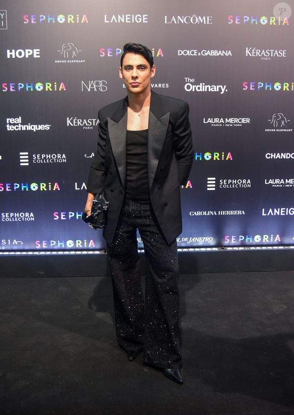 Theodoro apostou no clássico 'all black' com um toque de brilho noturno e sofisticação. O influenciador veste um blazer de lapela acetinada sobre uma regata preta básica, deixando o foco total para a calça de modelagem ampla inteiramente recoberta por microcristais que refletem a luz de forma sutil. O visual é arrematado por botas de bico fino e uma clutch estruturada preta, mantendo uma elegância moderna e urbana