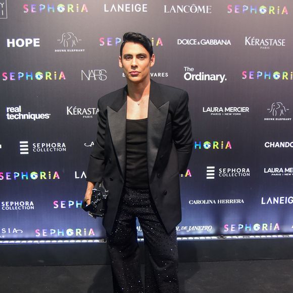 Theodoro apostou no clássico 'all black' com um toque de brilho noturno e sofisticação. O influenciador veste um blazer de lapela acetinada sobre uma regata preta básica, deixando o foco total para a calça de modelagem ampla inteiramente recoberta por microcristais que refletem a luz de forma sutil. O visual é arrematado por botas de bico fino e uma clutch estruturada preta, mantendo uma elegância moderna e urbana