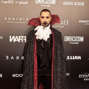 Gil do Vigor veste uma fantasia temática de vampiro clássico. O visual conta com fato e colete pretos, gola alta de renda branca franzida com joia central e uma longa capa preta cravejada de brilhos com o interior e gola estruturada em vermelho cintilante. Ele completa o look com mocassins pretos e maquilhagem facial marcada