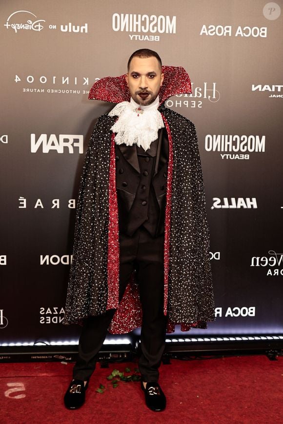 Gil do Vigor veste uma fantasia temática de vampiro clássico. O visual conta com fato e colete pretos, gola alta de renda branca franzida com joia central e uma longa capa preta cravejada de brilhos com o interior e gola estruturada em vermelho cintilante. Ele completa o look com mocassins pretos e maquilhagem facial marcada