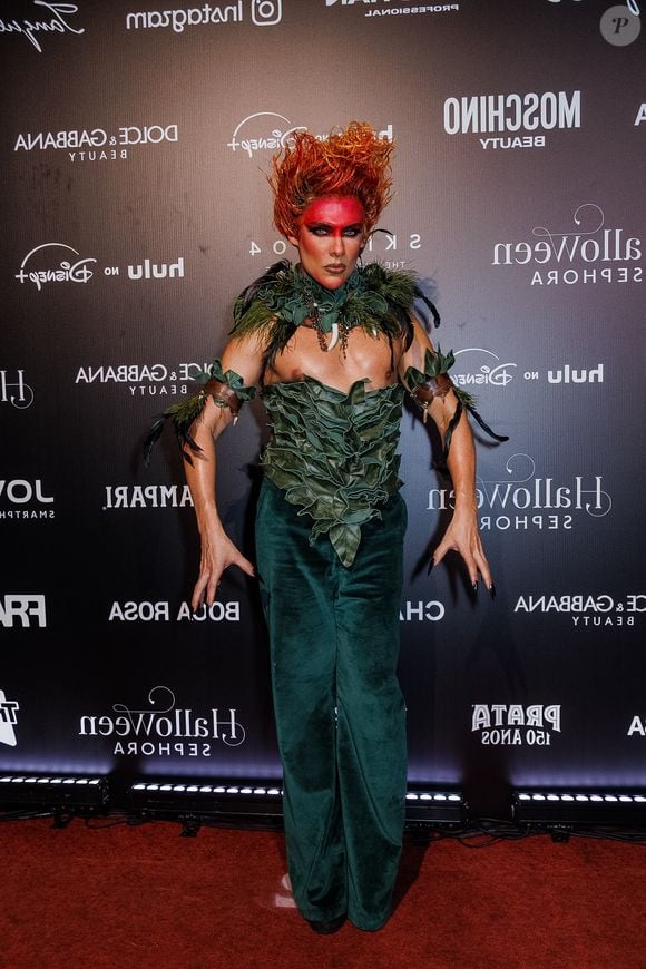 Theodoro, com inspiração no Curupira, veste um conjunto composto por calça de veludo verde-escuro e um top estruturado feito por folhagens esculpidas sobre o peitoral. O visual é complementado por uma gola com folhagens e dentes/garras decorativas, braçadeiras com tiras e folhagens, unhas compridas pretas, maquiagem facial vermelha ao redor dos olhos e cabelo eriçado em tom avermelhado