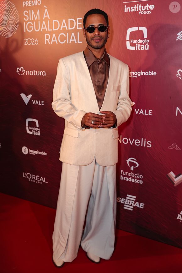 Ícaro Silva trouxe leveza e frescor ao tapete vermelho com uma proposta em tons de branco e off-white. O ator veste uma camisa de cetim branca com caimento fluido, gola aberta e barra assimétrica, combinada com uma calça de corte reto que apresenta pequenos bordados verdes espalhados pelo tecido
