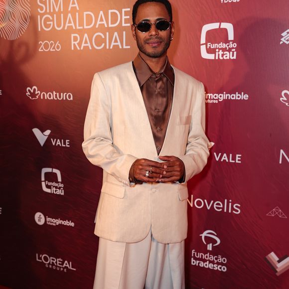 Ícaro Silva trouxe leveza e frescor ao tapete vermelho com uma proposta em tons de branco e off-white. O ator veste uma camisa de cetim branca com caimento fluido, gola aberta e barra assimétrica, combinada com uma calça de corte reto que apresenta pequenos bordados verdes espalhados pelo tecido