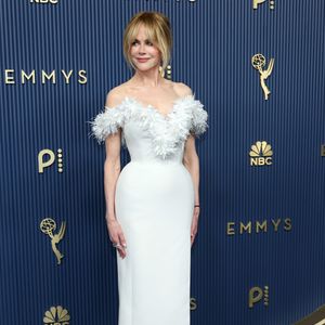 Nicole Kidman optou pela elegância atemporal de um vestido ajustado branco de comprimento midi com caimento estruturado e fenda discreta. O grande destaque da peça é o decote ombro a ombro adornado por plumas delicadas em tom sobre tom que emolduram o colo. Ela finalizou a produção com scarpins pretos clássicos de salto alto, coque despojado com franja solta e maquiagem de acabamento natural