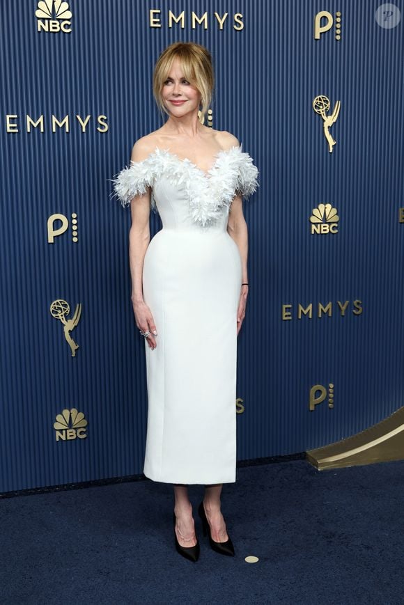 Nicole Kidman optou pela elegância atemporal de um vestido ajustado branco de comprimento midi com caimento estruturado e fenda discreta. O grande destaque da peça é o decote ombro a ombro adornado por plumas delicadas em tom sobre tom que emolduram o colo. Ela finalizou a produção com scarpins pretos clássicos de salto alto, coque despojado com franja solta e maquiagem de acabamento natural