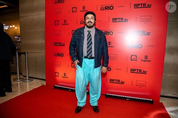 Luis Lobianco: O ator apresenta um look urbano e conceitual composto por jaqueta jeans escura sobre camisa social listrada com gravata tradicional azul e amarela. O visual ganha destaque com uma calça de sarja oversized azul-turquesa, boina preta clássica e sapatos de couro escuros