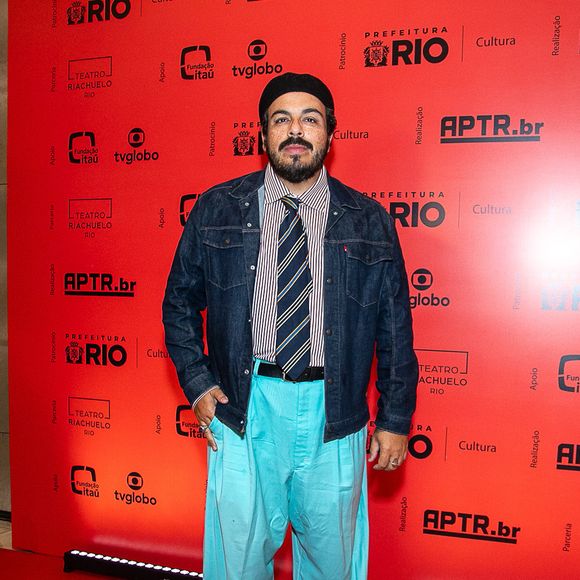 Luis Lobianco: O ator apresenta um look urbano e conceitual composto por jaqueta jeans escura sobre camisa social listrada com gravata tradicional azul e amarela. O visual ganha destaque com uma calça de sarja oversized azul-turquesa, boina preta clássica e sapatos de couro escuros