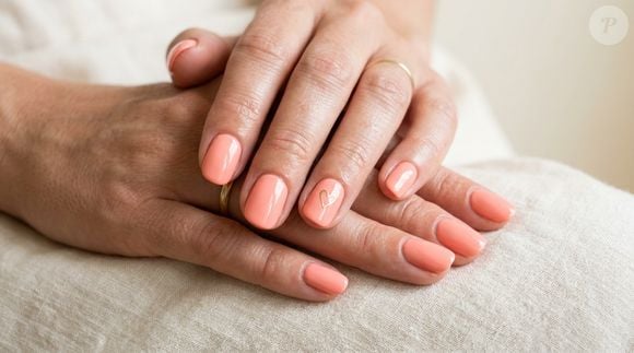A manicure coral pode ganhar um detalhe romântico com um pequeno coração em apenas uma das unhas, alternativa simples para personalizar o visual feito em casa