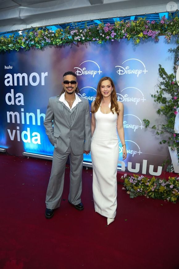 Sérgio Malheiros e Sophia Abrahão: o casal posa em sintonia no tapete vermelho; ele com costume cinza oversized, colete e óculos escuros, e ela com o vestido longo branco minimalista de decote halter e scarpin de bico fino