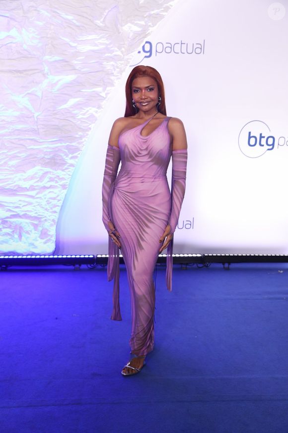 Gaby Amarantos: Vestido longo drapeado e ajustado ao corpo em tom lilás com efeitos sombreados em degradê cinza. O modelo possui decote de um ombro só com recorte assimétrico no colo, acompanhado de mangas longas independentes estilo luva que se estendem até o chão