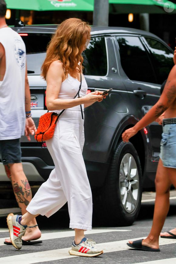 Macacão all white, bolsa laranja e listra alaranjada no tênis criam combinação harmônica com as madeixas ruivas da atriz