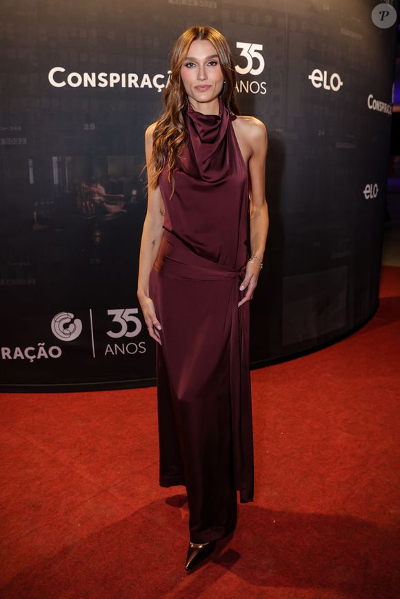 A paleta intensa também apareceu no look de Sasha Meneghel, que surgiu com vestido longo em tom vinho de acabamento acetinado. Com decote halter e gola drapeada, a peça valoriza o colo e aposta em caimento fluido, com amarração lateral que desenha a silhueta de forma delicada. O visual é elegante sem esforço - daqueles que funcionam justamente pela simplicidade bem executada!