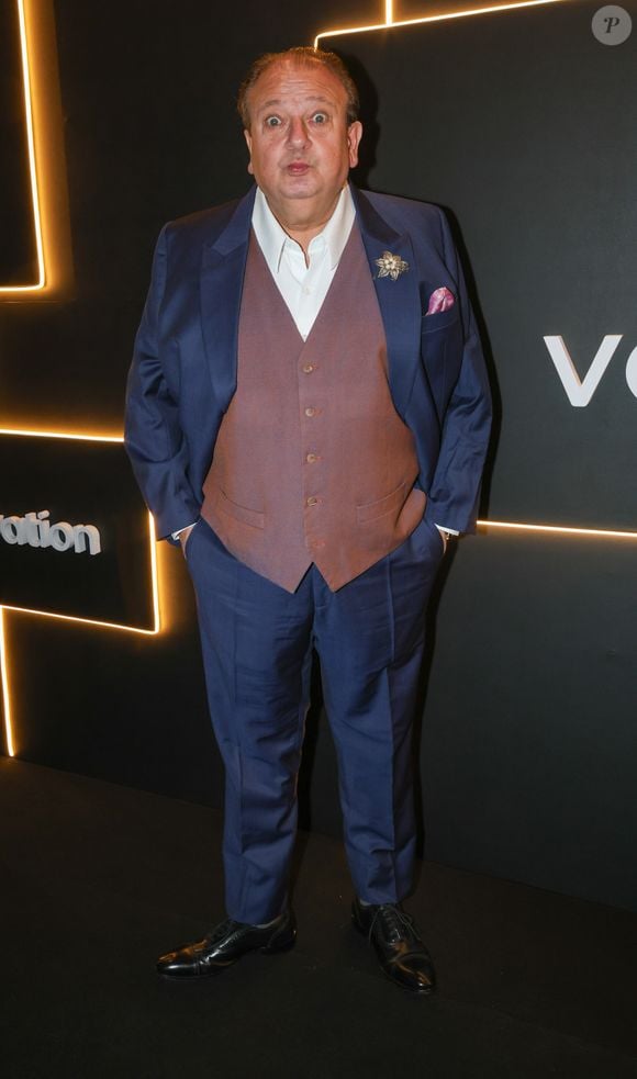 O renomado chef e jurado de TV Érick Jacquin mantém sua assinatura de elegância clássica francesa com um toque de personalidade. Ele comparece ao evento vestindo um terno de três peças composto por um paletó e calça em tecido azul-safira vibrante, contrastado por um colete social abotoado em tom de marrom-rosado acinzentado. Por baixo, uma camisa social branca de colarinho aberto sem gravata mantém o visual imponente porém confortável. Fiel aos detalhes, Jacquin adorna a lapela com um broche floral prateado com pérolas e insere um lenço de bolso rosa-antigo, completando o visual com sapatos sociais oxford pretos de couro legítimo
