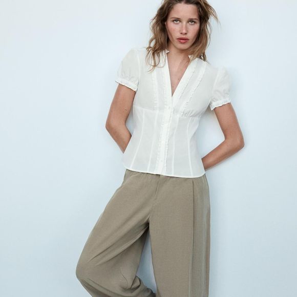 Com modelagem ajustada, a Camisa de Popelina com Abertura e Laços da Zara combina gola redonda, mangas curtas, forro interno e fechamento com botão oculto e laços