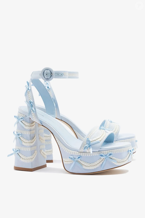 Quem procura um salto diferente para casamentos e festas pode encontrar uma alternativa na nova Larroudé x Tanner Fletcher: Sandália Dolly Cake & Lace Cetim Azul. Com salto bloco de 11,5 centímetros e plataforma de 4 centímetros, o modelo une altura, estabilidade e um visual inspirado na estética coquette