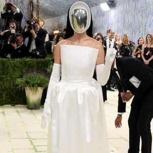 Katy Perry escolheu um visual minimalista e futurista, composto por um vestido tomara-que-caia branco acetinado e luvas longas, tendo como ponto focal uma máscara facial prateada espelhada que cobria completamente seu rosto