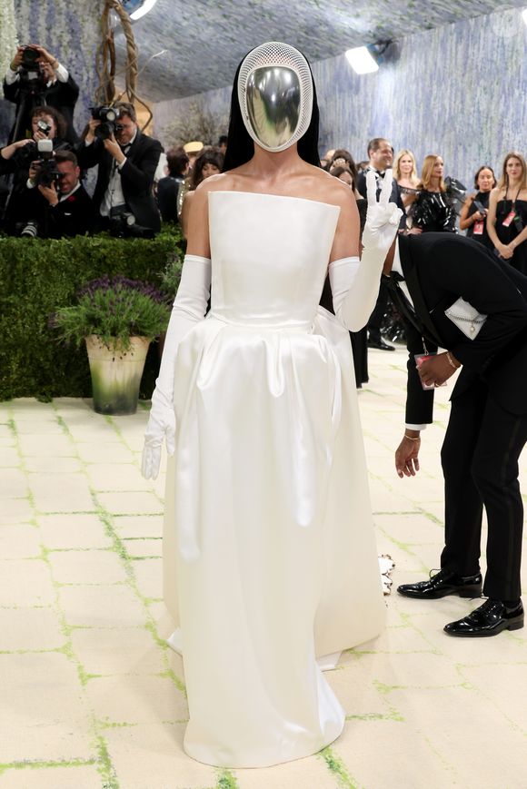 Katy Perry escolheu um visual minimalista e futurista, composto por um vestido tomara-que-caia branco acetinado e luvas longas, tendo como ponto focal uma máscara facial prateada espelhada que cobria completamente seu rosto