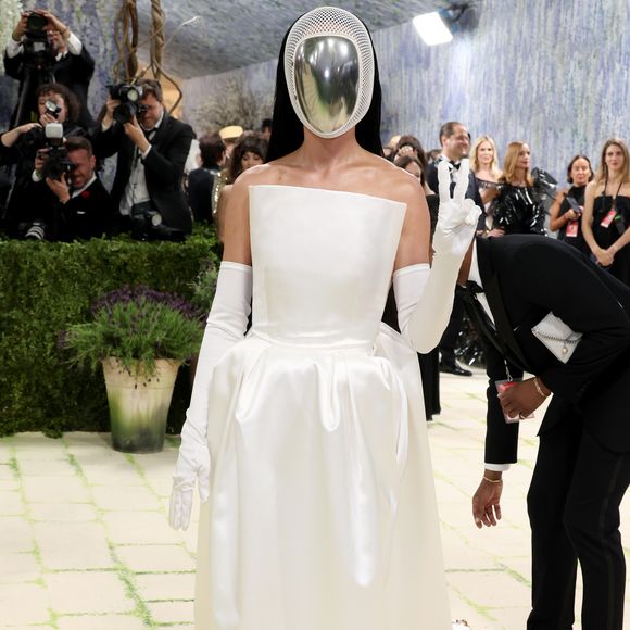 Katy Perry escolheu um visual minimalista e futurista, composto por um vestido tomara-que-caia branco acetinado e luvas longas, tendo como ponto focal uma máscara facial prateada espelhada que cobria completamente seu rosto