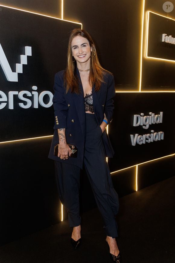 A jornalista Mari Palma traz uma proposta urbana e despojada, equilibrando a sofisticação da alfaiataria com a sensualidade da lingerie exposta. Ela usa um terno azul-marinho de corte solto, composto por um blazer de abotoamento duplo com botões dourados decorativos e mangas sutilmente puxadas, além de uma calça de alfaiataria de cintura alta com estampa sutil de risca-de-giz e barra levemente afunilada. Sob o blazer aberto, destaca-se um top estilo cropped de renda preta trabalhada