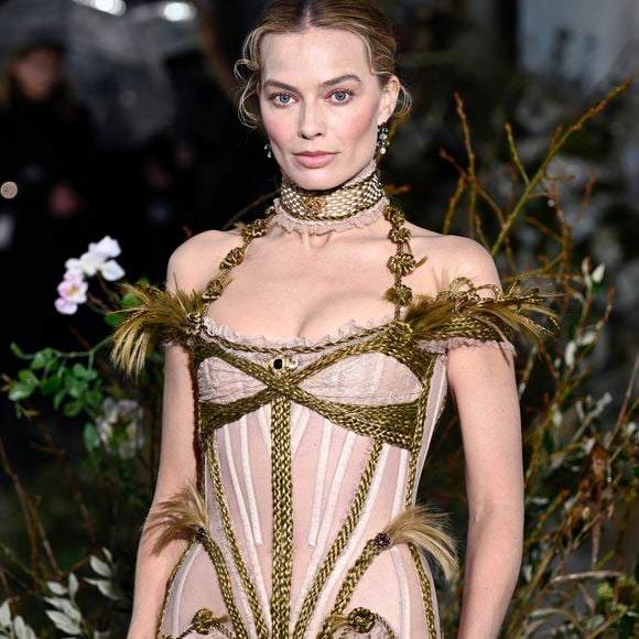 O look de Margot Robbie na première reforçou a narrativa do filme: vestido nude de estética vitoriana, criado por Dilara Findikoglu, em sintonia com a joia histórica escolhida para a ocasião