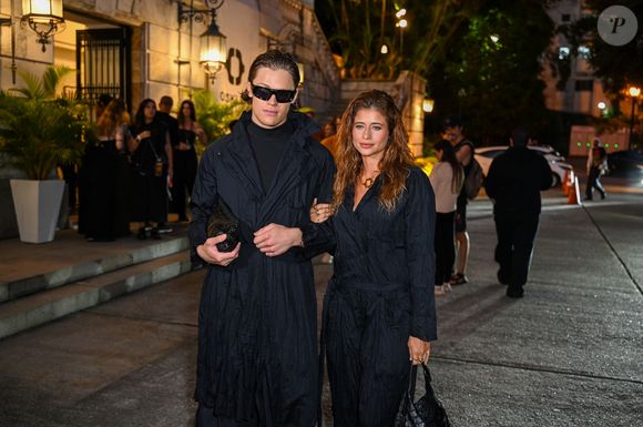 Ao seu lado, Lucas Pinheiro radicaliza no volume com uma capa oversized de nylon técnico sobre uma base de gola alta e calças pantalonas extremamente amplas, que tocam o chão. O visual de Lucas é finalizado com óculos de sol futuristas e uma clutch de couro texturizado, reforçando uma estética nômade urbana de vanguarda