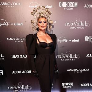 Medusa? Juliana Paes veste um vestido midi preto justo com mangas bufantes volumosas e recortes no busto, revelando um sutiã de renda preto por baixo. Ela usa luvas de ópera pretas, meia-calça de renda floral preta e sapatos de salto alto pretos de bico fino. O grande destaque é o adereço de cabeça dourado intrincado, composto por várias flores e filigranas douradas que criam um efeito de coroa imponente