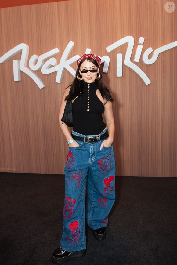 Ana Hikari apostou em um look que mistura referências fashion e streetwear. Ela combinou uma regata preta de gola alta com recortes e calça jeans oversized estampada com desenhos vermelhos