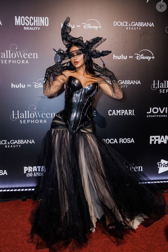 Mileide Mihaine: o look apresenta uma estética gótica e dramática. É composto por um corpete justo e estruturado em material preto envernizado com brilho e texturas lineares. A parte inferior é uma saia longa e volumosa de baile com camadas sobrepostas de tule preto e nude, criando profundidade e movimento