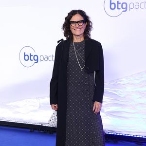 Zélia Duncan: Look moderno composto por um casaco alongado (estilo sobretudo leve) em tom verde-oliva com lapelas largas, usado sobre blusa preta de gola alta e calça social preta de modelagem reta, finalizado com sapatos pretos fechados de bico fino