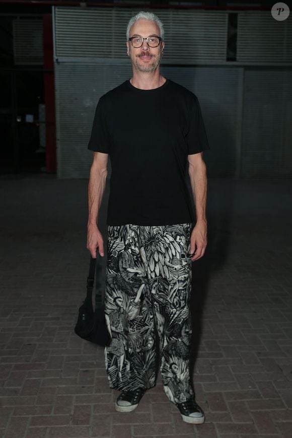 Guilherme Weber apostou em uma produção conceitual ao destacar uma calça de modelagem ampla com estampa gráfica em preto e branco com motivos artísticos. Ele equilibrou a peça chamativa com uma camiseta preta básica de gola careca e mangas curtas. O ator completou o visual com tênis preto estilo All Star, óculos de armação marcante e uma bolsa tira-colo tirada a tiracolo