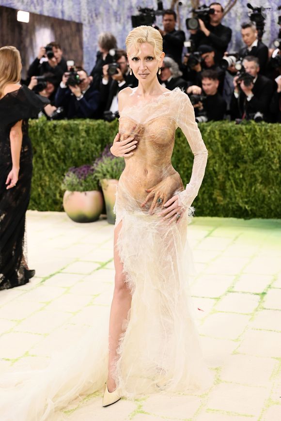 Sabine Getty exibiu um vestido transparente em tom nude com efeito 'molhado' e texturizado, apresentando detalhes surrealistas de mãos esculpidas que parecem envolver seu corpo estrategicamente
