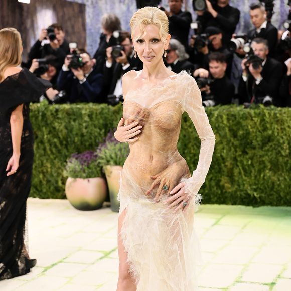 Sabine Getty exibiu um vestido transparente em tom nude com efeito 'molhado' e texturizado, apresentando detalhes surrealistas de mãos esculpidas que parecem envolver seu corpo estrategicamente