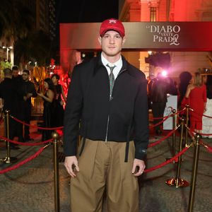 Pedro Novaes, o Léo de 'Três Graças', quebrou totalmente o protocolo formal com uma estética urbana e utilitária. Ele combinou uma jaqueta preta de corte cropped com zíper frontal e camisa branca com gravata estampada. O destaque do look foram as calças baggy de sarja cáqui, extremamente volumosas, e o boné vermelho da marca Chicago Bulls, que serviu como o ponto de cor focal da produção, finalizada com botas de sola tratorada