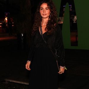 A atriz Nanda Costa investe no pretinho nada básico com um visual all black fluido, composto por uma blusa texturizada transpassada de decote em V profundo e calça pantalona de modelagem ampla com caimento pesado. Os acessórios incluem uma bolsa transversal preta com alça de corrente e discretas pulseiras prateadas em ambos os pulsos