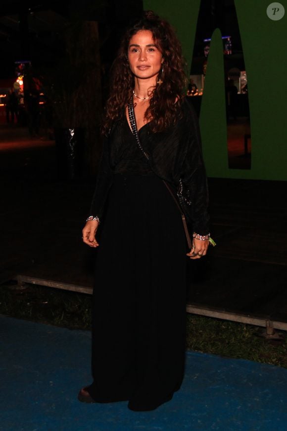 A atriz Nanda Costa investe no pretinho nada básico com um visual all black fluido, composto por uma blusa texturizada transpassada de decote em V profundo e calça pantalona de modelagem ampla com caimento pesado. Os acessórios incluem uma bolsa transversal preta com alça de corrente e discretas pulseiras prateadas em ambos os pulsos