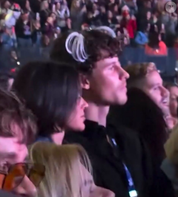 Shawn Mendes optou por uma composição minimalista na plateia, vestindo uma camisa ou jaqueta preta de abotoamento frontal e carregando também sua credencial de acesso, enquanto ostenta as clássicas chuquinhas brancas estilo Xuxa presas ao cabelo cacheado